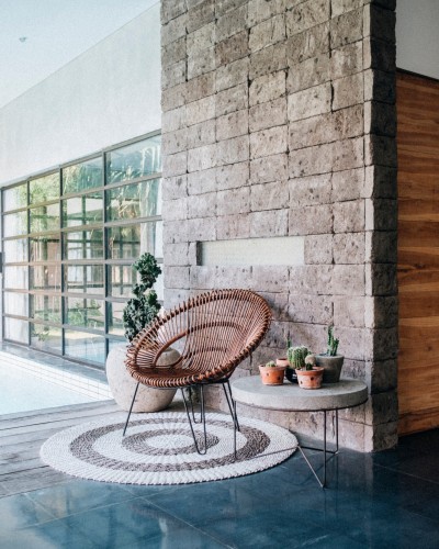 Cadeira de vime castanho, tapete redondo branco e castanho, mesa de centro com vasos de cactos, planta decorativa grande