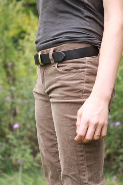 Pessoa com calças de veludo castanhas, cinto preto e camiseta cinzenta