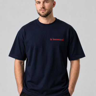 Homem com t-shirt azul escuro com texto vermelho e calças pretas em fundo cinzento.
