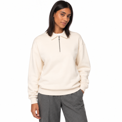Mulher com camisola creme de manga comprida e fecho metálico, calças cinza, fundo branco