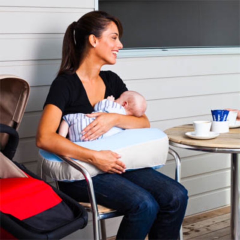 Almofada de aleitamento Fertile Mind Milkbar® Pillow Mulher a amamentar bebé com almofada azul e cinza numa cadeira ao lado de mesa com chávenas