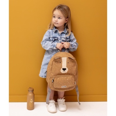 Mochila infantil castanha com rosto de urso segurada por menina em vestido de ganga azul