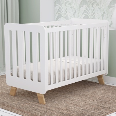 Berço de bebé branco com pernas de madeira clara sobre tapete castanho