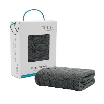 Cobertor de malha cinzento dobrado ao lado da embalagem branca com janela e alça azul