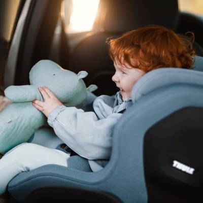 Cadeira auto cinza com criança ruiva e ursinho verde num carro