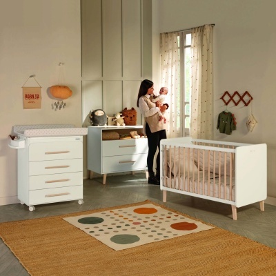 Quarto de bebé com mobiliário branco e madeira clara, tapete colorido e mulher a segurar bebé