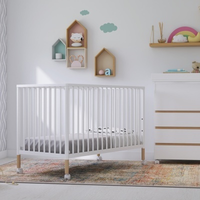 Berço branco de madeira com rodas junto a paredes decoradas com prateleiras e tapete colorido