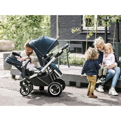 Carrinho de bebé azul escuro com estrutura prateada e rodas pretas num parque urbano