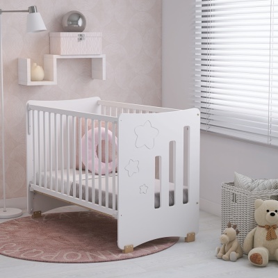 Berço de madeira branco com estrelas decorativas, tapete rosa, almofada rosa, brinquedos e janela com persianas brancas