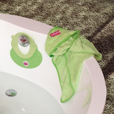 Toalha de bebé verde clara sobre borda branca de banheira com válvula e suporte verde claro.