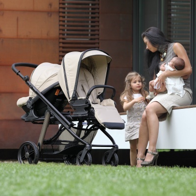 Carrinho de bebé duplo bege com estrutura preta em relvado urbano