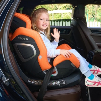 Cadeira auto infantil Recaro preta e laranja no banco traseiro de carro com criança sorridente