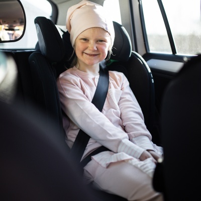 Criança sorridente sentada numa cadeira auto preta com cinto de segurança no carro