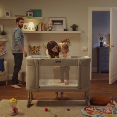 Berço portátil cinzento Chicco com crianças e adultos numa sala de estar