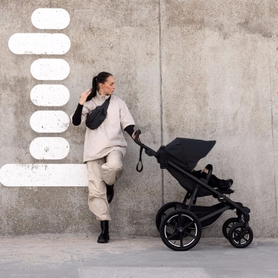 Carrinho de bebé preto com quatro rodas grandes e mulher ao lado