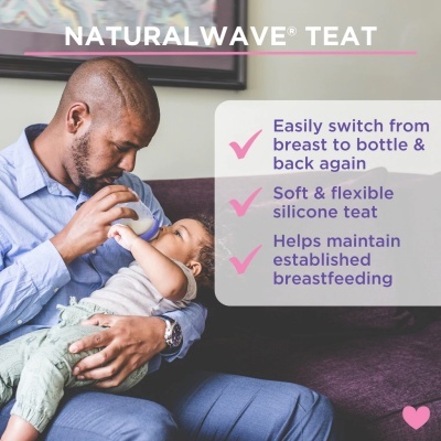 Pai a dar mamadeira com tetina NaturalWave a bebé sentado em sofá roxo