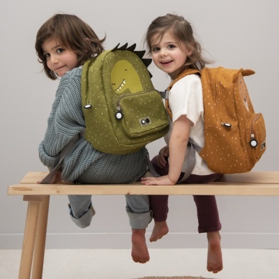 Duas crianças sentadas com mochilas coloridas, verde com dinossauro e laranja com pintas brancas