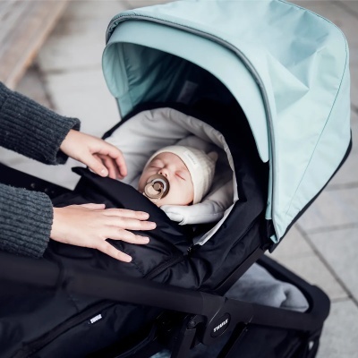 Bebé adormecido num carrinho preto com capota azul clara, com mãos de adulto ajustando cobertor