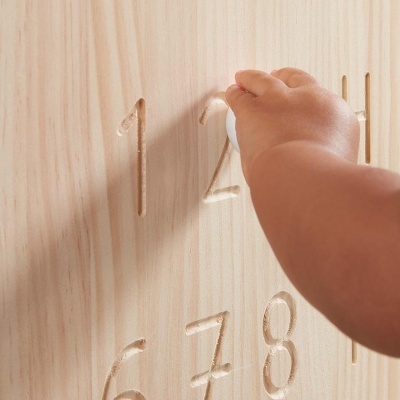 Mão de criança a tocar números em relevo numa placa de madeira