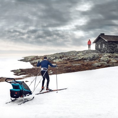 Pessoa a praticar esqui de fundo na neve com cabana de pedra ao fundo
