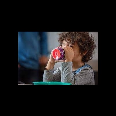 Criança a beber de caneca vermelha translúcida num ambiente interior