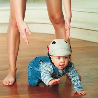 Criança a engatinhar com capacete cinzento num chão de madeira
