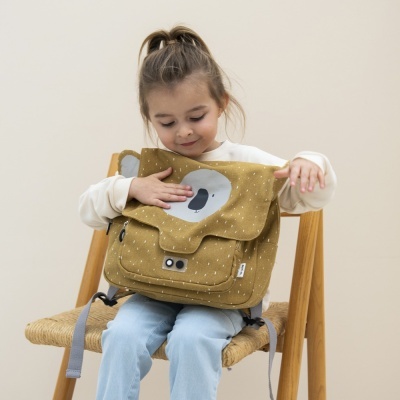 Menina sentada numa cadeira com mochila castanha com padrão e rosto de urso.