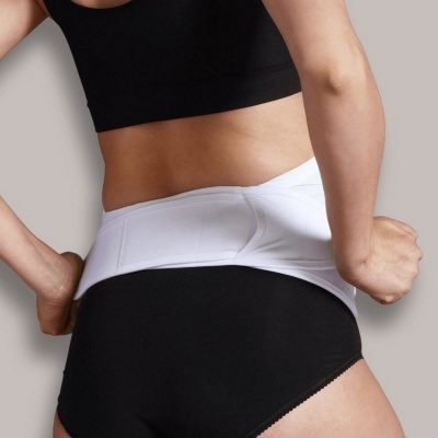 Mulher a usar cinta modeladora branca sobre cuecas pretas e top preto