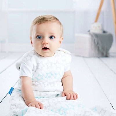 Bebé com saco de dormir branco com estrelas sentado em chão branco