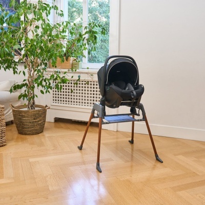 Cadeira alta para bebé preta com pernas de madeira numa sala com planta e janela.