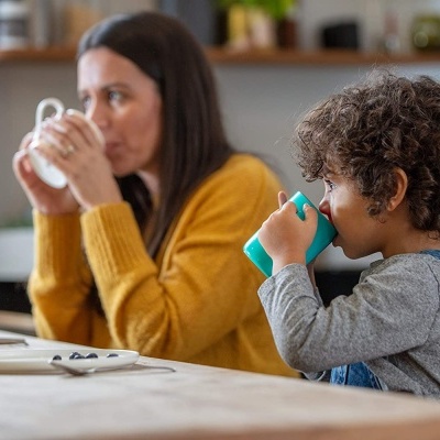 Criança e mulher a beber de canecas numa cozinha moderna