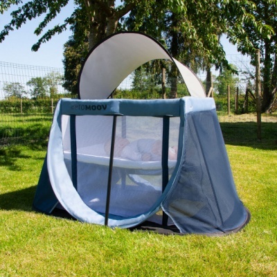 Berço de viagem azul claro com laterais em rede num jardim verde