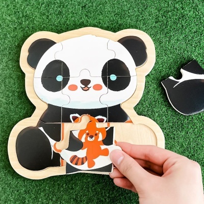 Puzzle de madeira em forma de panda com uma peça com imagem de urso vermelho sendo colocada.
