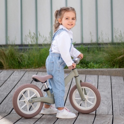 Menina pequena com bicicleta de equilíbrio cinzenta numa área exterior de madeira