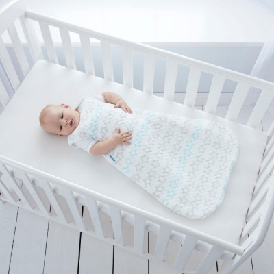 Bebé num saco de dormir com padrão de estrelas num berço branco.
