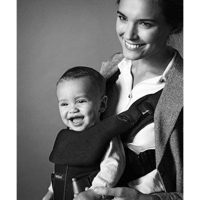 Mãe a usar canguru preto com bebé sorridente ao peito