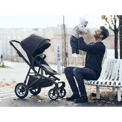 Carrinho de bebé preto com homem a segurar bebé junto a banco branco