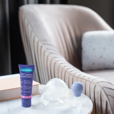 Creme Lansinoh HPA Lanolin Nipple Cream e acessórios para amamentação sobre mesa branca junto a poltrona cinzenta
