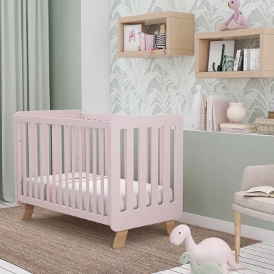 Berço rosa claro com colchão branco em quarto decorado com tapete castanho e prateleiras de parede com brinquedos e livros