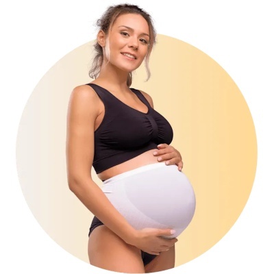 Mulher grávida com top desportivo preto e cuecas segurando a barriga com fundo amarelo claro