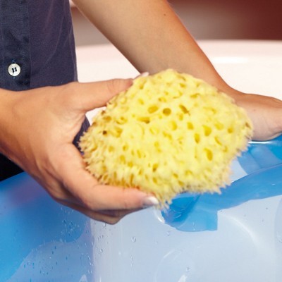 Esponja natural amarela nas mãos sobre balde azul com água