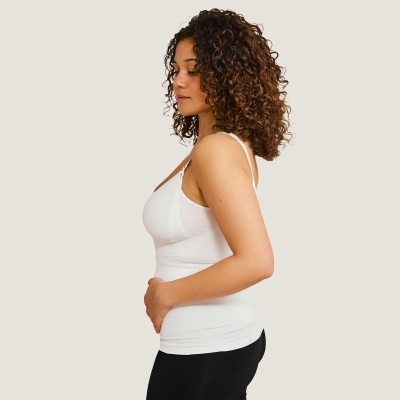 Mulher de perfil com camisola branca e leggings pretas em fundo bege claro