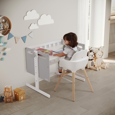 Criança sentada em cadeira branca à frente de secretária infantil cinzenta numa sala decorada para crianças