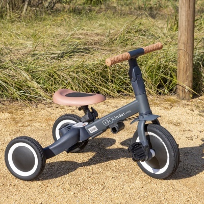 Triciclo infantil cinza com assento castanho e rodas pretas com borda branca em chão de terra