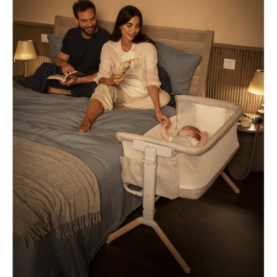 Berço de bebé junto à cama com revestimento bege e branco e estrutura metálica e pernas de madeira