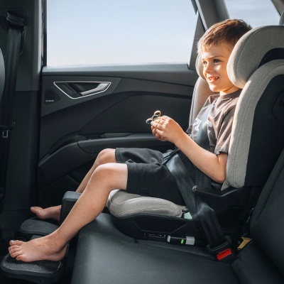 Criança numa cadeira auto cinzenta num carro, a segurar um spinner prateado