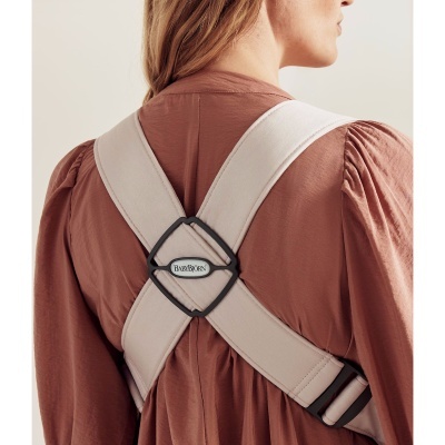 Correia cruzada bege com etiqueta BABYBJÖRN usada sobre camisa rosa com mangas bufantes