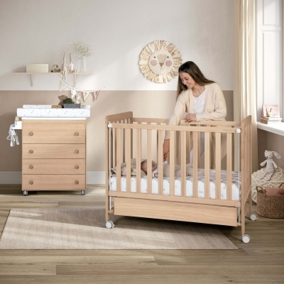Berço de madeira clara com cómoda de troca e mulher com bebé