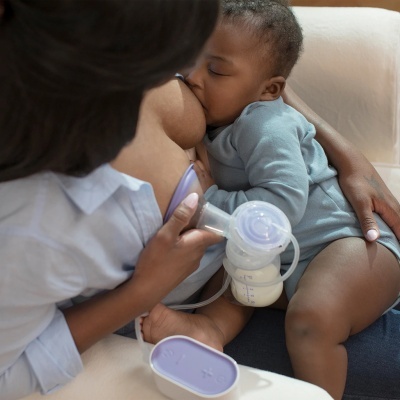 Bomba de extração de leite com bebé a mamar no colo da mãe