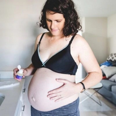 Mulher grávida de soutien preto e calças listradas segurando frasco pequeno em interior